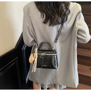 Detail of black glossy handbag with wrinkled texture and cute bear charm on gray blazer