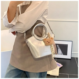 Detail of silver metallic bucket bag with round hollow handle and plush bear charm