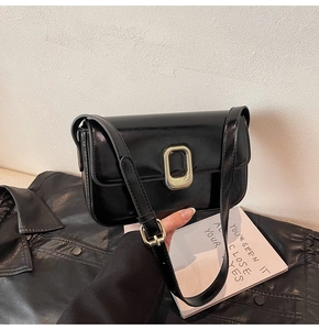 Detalle de un bolso de hombro de cuero negro brillante con hebilla ovalada de metal dorado