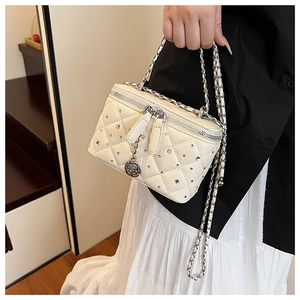 Detailed macro view of beige quilted box bag featuring silver studs and floral charm