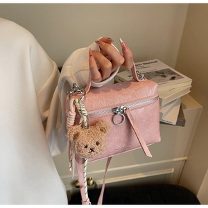 Close-up of pink textured bucket bag featuring silver ring zipper and plush bear charm