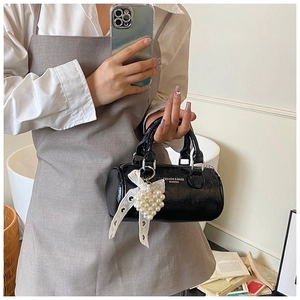 Detail of black cylinder bag with white lace bow and pearl heart pendant handle
