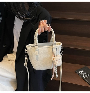 Close-up of white lychee-patterned bucket bag with silver rings and plush bear charm