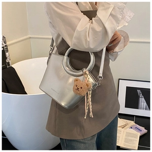 Detail of silver bucket bag with circular handle, plush bear charm and striped ribbon