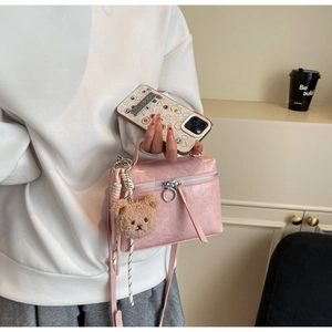 Detail of pink bucket bag with crinkled texture, plush bear charm and metallic zipper