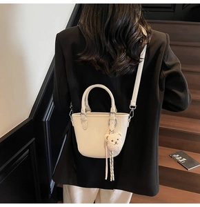 Detail of off-white lychee grain leather mini bucket bag with a plush bear charm