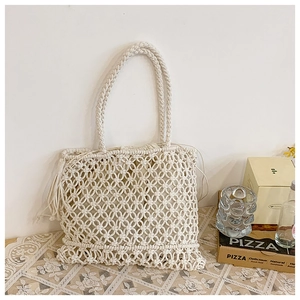 Detail of white woven straw tote bag featuring tassel charm and drawstring liner pouch