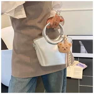 Detail of silver bucket bag with plush bear charm and metallic finish shown by model