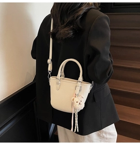 Detail of cream lychee texture leather bucket bag with cute white plush bear pendant