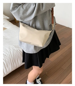 Detail of beige nylon crossbody bag with brown leather strap and gold hardware accents
