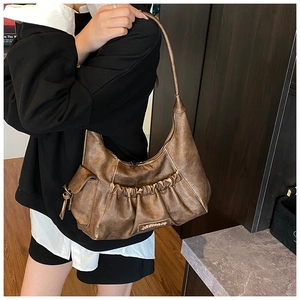 Close-up of retro brown pleated hobo bag with vintage leather texture and metal logo detail