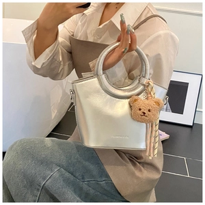 Detail of silver metallic bucket bag with metal handle, bear charm and ribbon decor