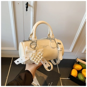 Detail view of a cream cylinder bag with pearl heart charm and lace bow decoration