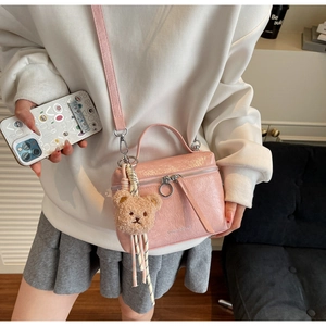 Detail of pink glossy crossbody bucket bag with bear pendant and double zipper closure