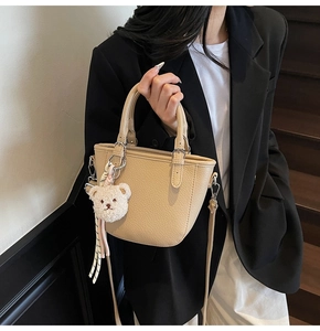 Detail of beige lychee pattern bucket bag with plush bear charm on a female model