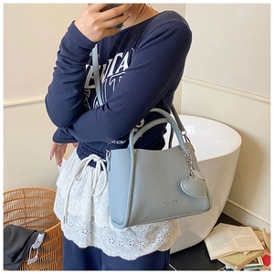 Detail of blue pebbled leather bucket bag featuring a heart charm and detachable strap