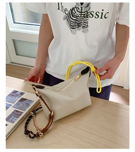 Detail of beige half-moon shoulder bag with yellow woven handle and chain strap