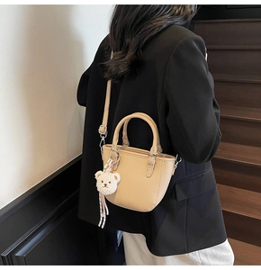 Close-up of beige lychee textured bucket bag with cute plush bear charm accessory