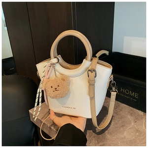 Detail of cream bucket bag featuring contrast khaki handles and plush bear charm