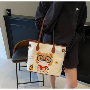 Detail of a beige tote bag featuring a cute cartoon bear and brown leather trim