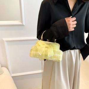 Close-up of woven tweed shell bag with organza bow and pearl accents on elegant metallic clasp
