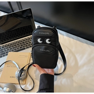 Detail of black mini crossbody bag with cartoon eyes and dual zipper pockets on desk