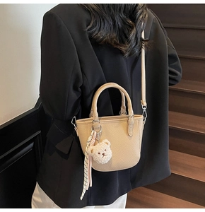 Detail of beige bucket bag with plush bear charm and scarf on model in black suit