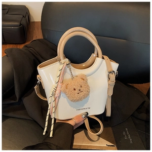 Detailed view of the white bucket bag with a plush bear charm and woven rope accent