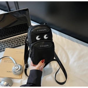 Close-up of black canvas crossbody phone bag featuring embroidered cartoon eyes detail