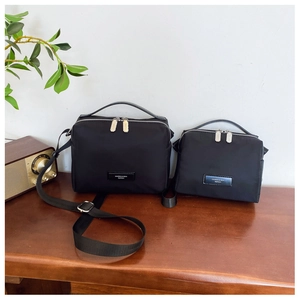 Détail de deux sacs bandoulière en nylon noir de tailles différentes sur une table en bois