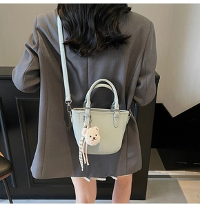 Close-up of mint green pebbled leather bag with plush bear charm and striped ribbon