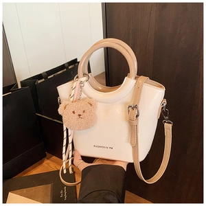Detail of a beige bucket bag with polished leather finish and cute bear pendant charm