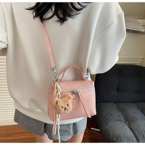 Pink mini crossbody bag with crackle texture and bear charm shown on a model