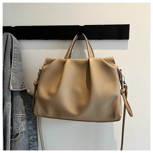 Detail of khaki pleated leather tote showing premium grain texture and handle on a wall hook