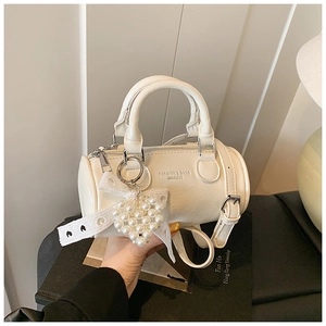 Close-up of cream white barrel bag with bow detail and heart pearl pendant