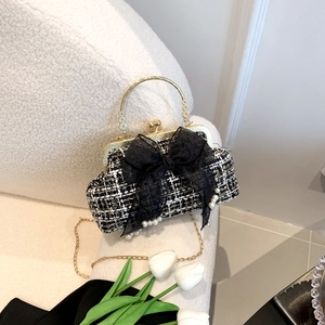Detail of tweed shell bag with black lace bow and elegant pearl charms on soft fabric