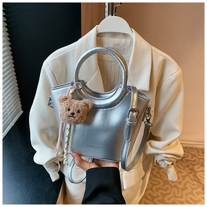 Silver bucket bag detail featuring metal ring handle and cute bear charm decoration