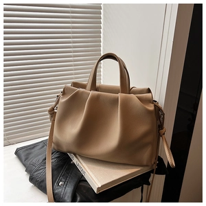 Detail of beige pleated leather bucket bag on books with light through shutters