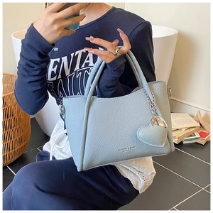Detail of light blue pebble grain leather handbag with heart charm and chain