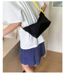 Detail of black nylon crossbody bag featuring bright yellow rope strap and gold metal hooks