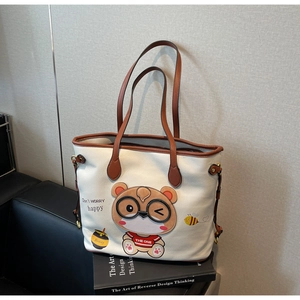 Detail of cream tote bag with cartoon bear patch and brown shoulder strap on a book