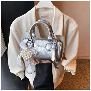 Detail of silver cylindrical handbag with ruffled leather texture and pearl heart charm