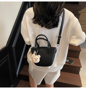 Close-up of black pebble texture handbag with plush bear charm and adjustable shoulder strap