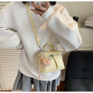 Detail of light yellow lychee leather bucket bag with cute bear charm and metal ring zipper