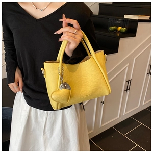 Detail of yellow lychee pattern leather tote bag with heart pendant on a model