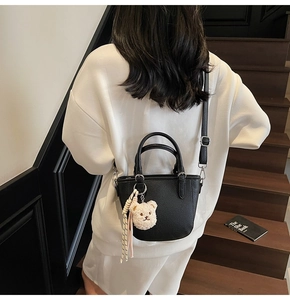 Side view of black lychee leather mini tote bag with plush charm and striped ribbon
