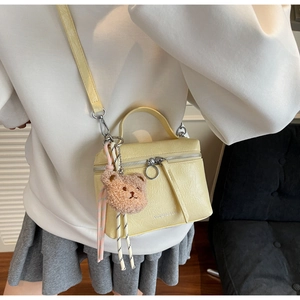 Detail of yellow mini bucket bag with soft texture and cute brown teddy bear charm
