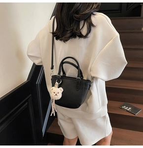 Detail showing black lychee grain bucket bag with a cute plush bear pendant accessory