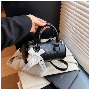 Detail of black cylindrical handbag with wrinkled texture and lace pearl charm