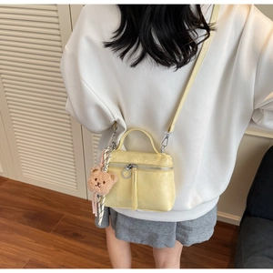 Back view of model wearing a pale yellow mini bucket bag with a plush bear charm
